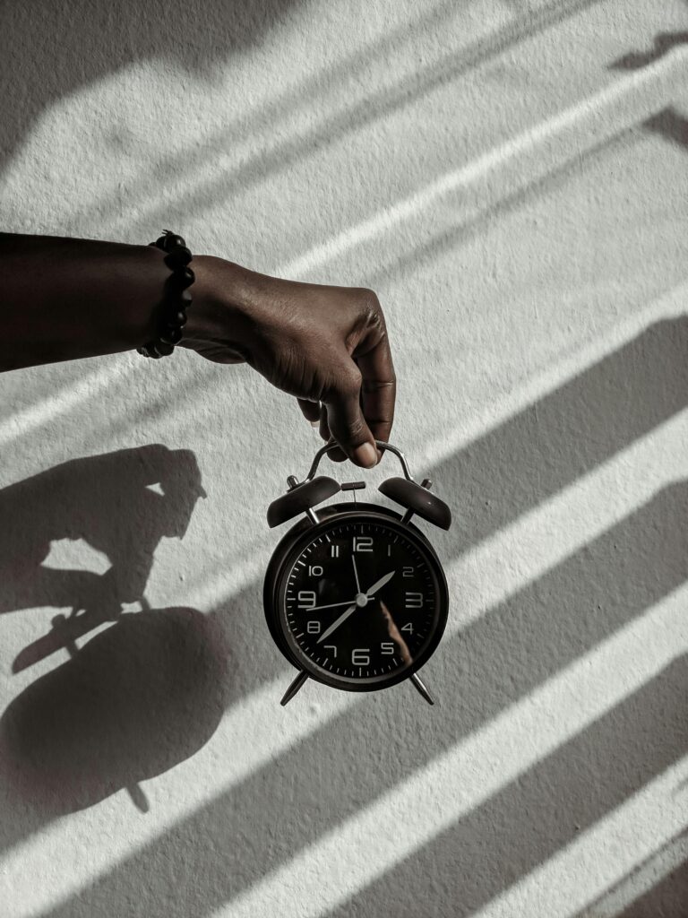 Close-up of a hand holding a vintage alarm clock casting shadows in daylight.
